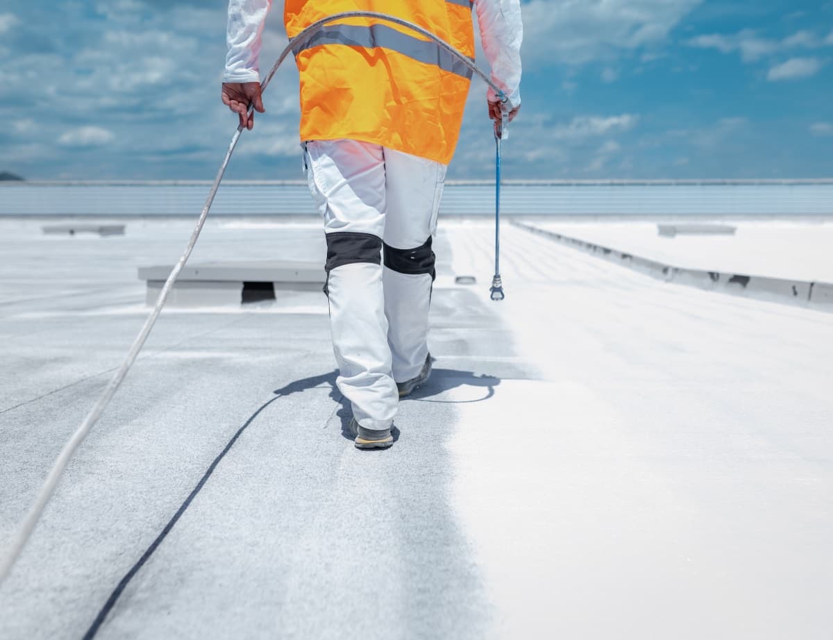 Peintre appliquant de la peinture reflective sur une toiture plate.