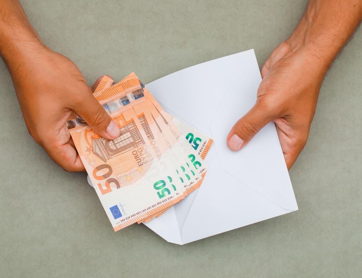 Gros plan sur des billets de 50 placés dans une enveloppe par un homme