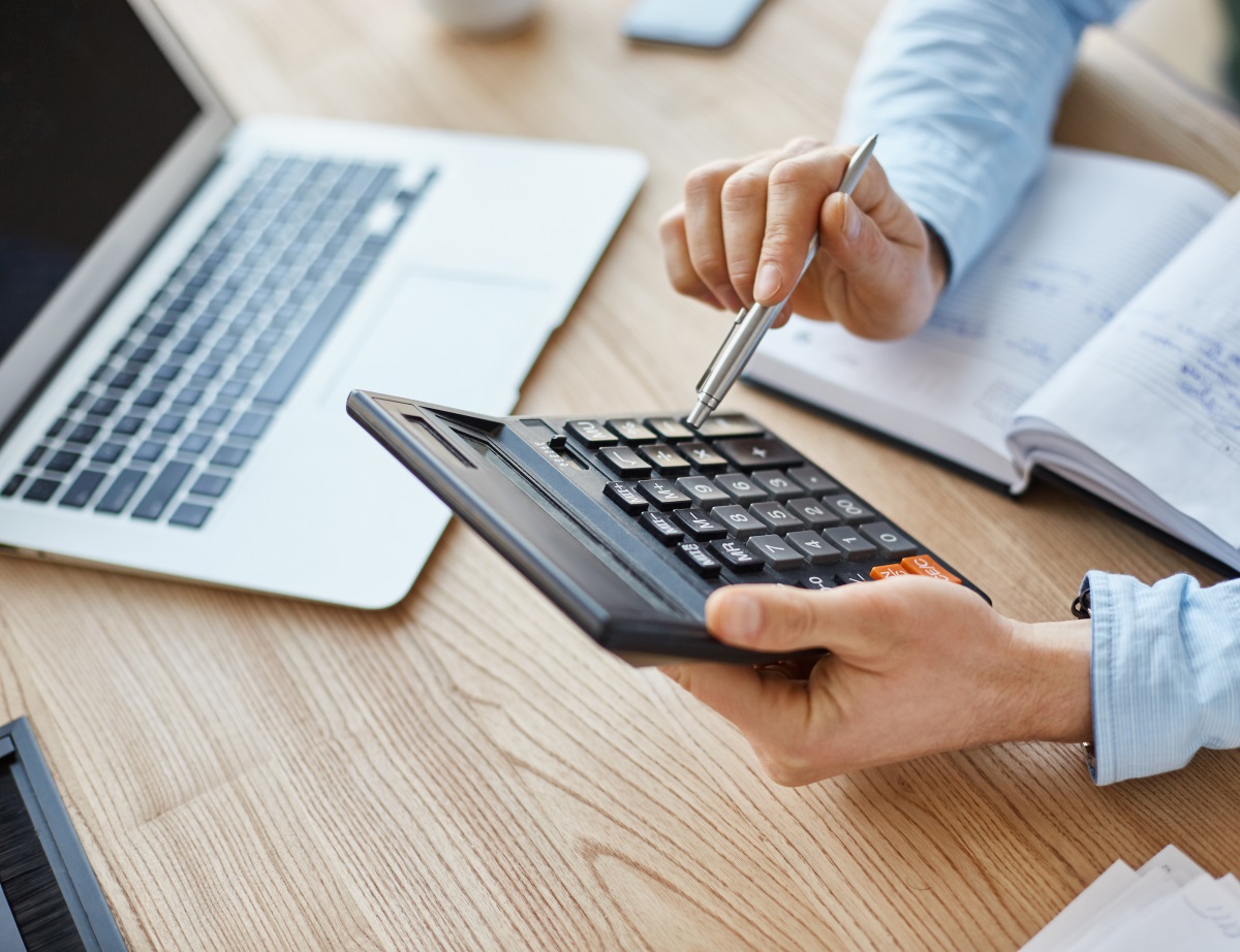 Mains en gros plan en train de faire un calcul à l'aide d'une calculatrice sur un bureau