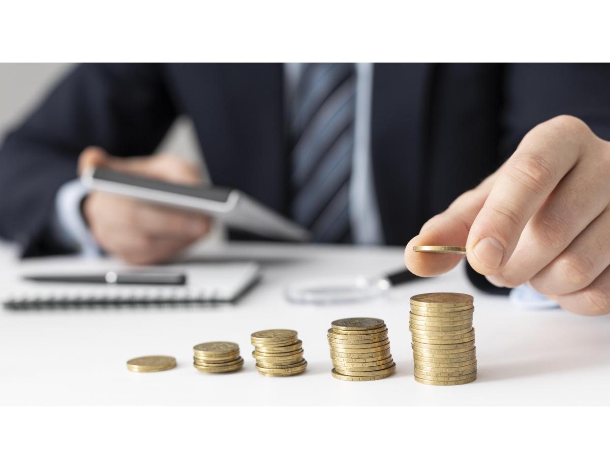 piles de pièces et homme qui fait ses comptes en arrière plan