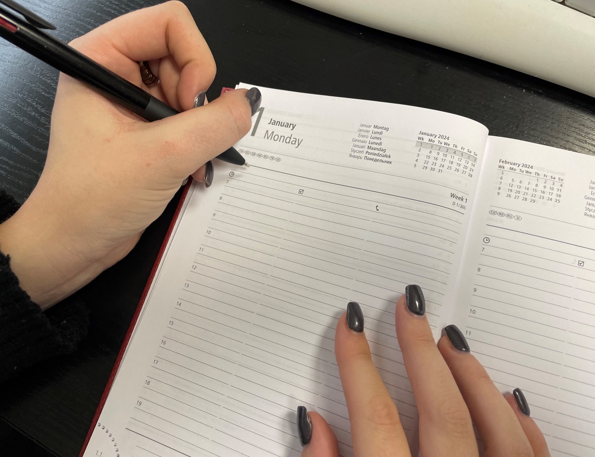 Une main tenant un stylo devant la page du 1er janvier 2024 d'un agenda.