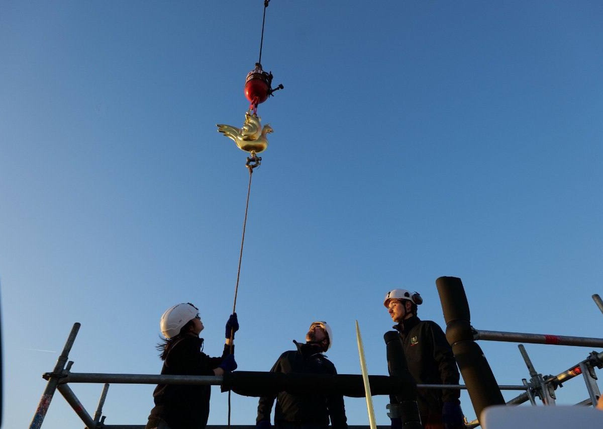 Le coq en train d'être fixé au sommet de l'édifice